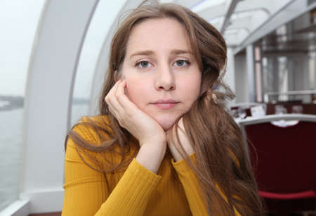 A girl with very long hair in a yellow turtleneck put her face thoughtfully in her arms in a cafeの写真素材