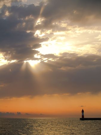 Sunset with visible sunrays in sea with lighthouseの写真素材