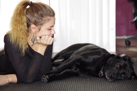 Teenage girl lying on the floor with a black dogの写真素材