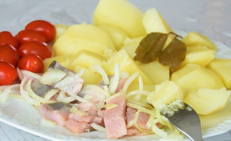 Herring fillet with onions, boiled potatoes, bay foxes and mini tomatoes on a white plateの写真素材
