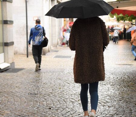 Girl in a fashionable coat is walking under umbrella on the streetの写真素材