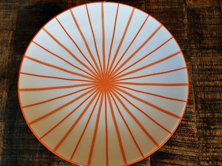 White plate with orange stripes on a wooden brown tableの写真素材
