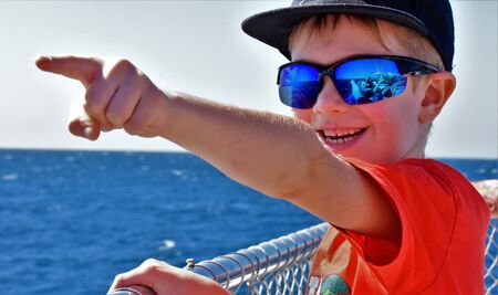 Boy in mirrored sunglasses is standing on a coral pi is pointing finger forward