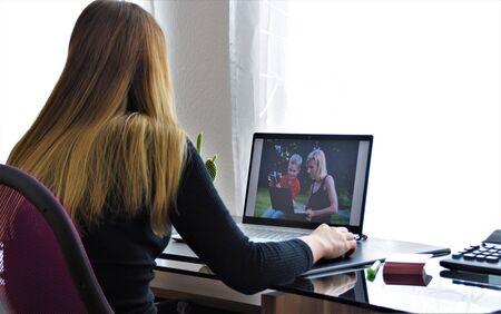 Girl with long hair sits at a desk and looks at a laptop