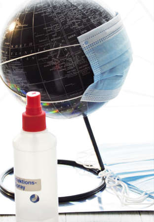 Black globe with a medical mask and disinfectant spray bottle on white