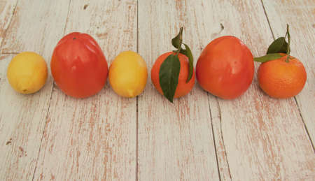 Lemons, tangerines, and persimmons in one row on a wooden table