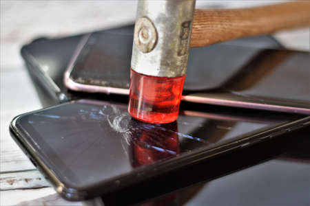 Close-up of a hammer hitting a smartphone with a red lighterの写真素材