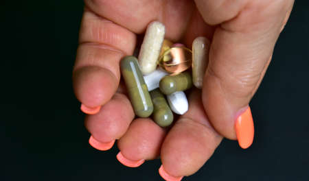 pills and capsules in a female palm on a black background