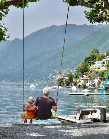 A man and a boy are sitting on a swing near the shore of the lakeの写真素材