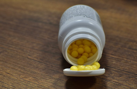 plastic vial with yellow pills on a wooden tableの写真素材