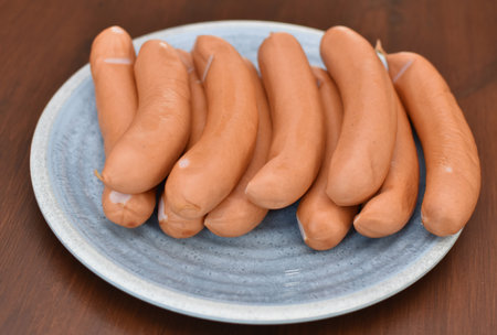 Meat sausages lie on a round blue plate on a wooden tableの写真素材
