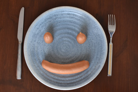 sausages on a plate and a fork with a knife on a wooden tableの写真素材