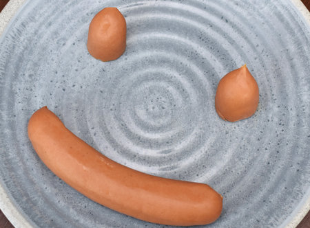 Meat sausages lie on a round blue plate on a wooden tableの写真素材