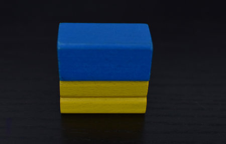 Wooden building blocks. Ukrainian flag on the cubes. Black background.