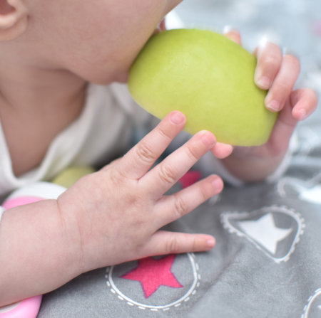 baby 6 months old with a green apple in his handの写真素材