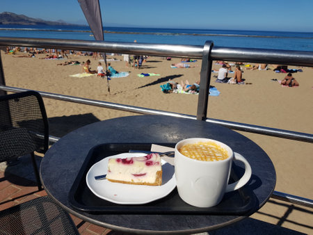 cappuccino and a piece of cake on a table near the boardwalk by the oceanの写真素材