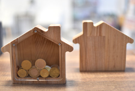 Wooden piggy bank in shape of house with euro coins on wooden table