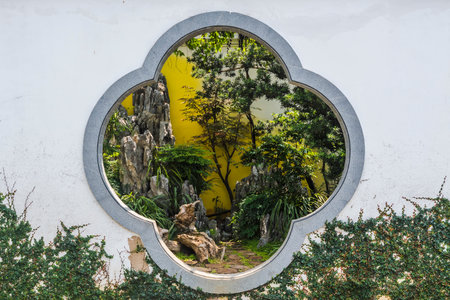 Round window on the wall of a house with green plants and treesの写真素材