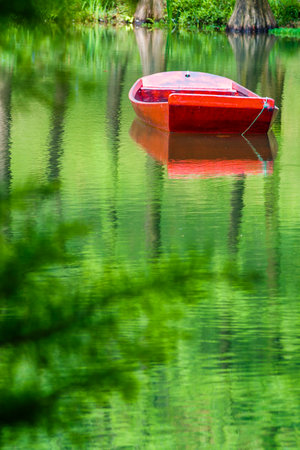 Red boat on the water with reflection of trees in the lake.の写真素材