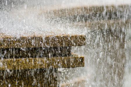 Water splashing on a wooden bench in a park, close upの写真素材