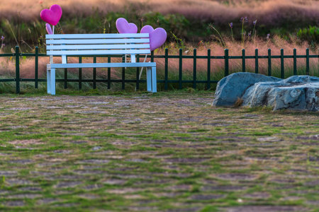 Pink heart shaped balloons on a bench in the park with a fenceの写真素材