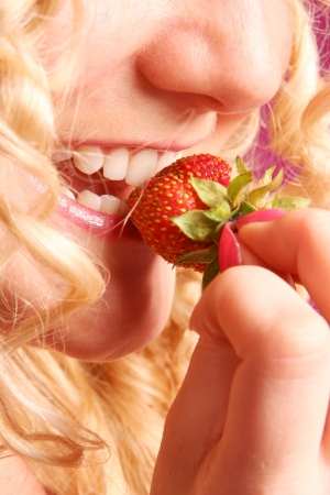 blonde curly girl biting strawberryの写真素材