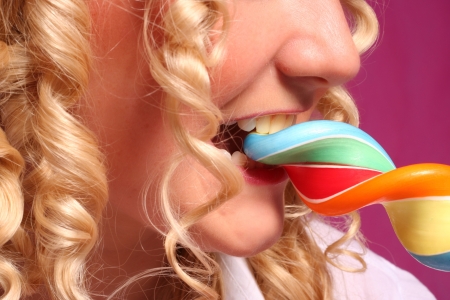woman with blonde curly hair biting bright lollipop  over pink background の写真素材