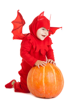little boy in red devil costume sitting near big pumpkin over white backgroundの写真素材