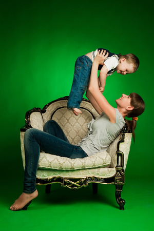happy mother holding her little boy up sitting in armchairの写真素材