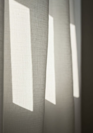 Natural sunlight streams through light fabric curtains, casting geometric shadows on the textured textile in a simple everyday domestic home interior background or design.の素材