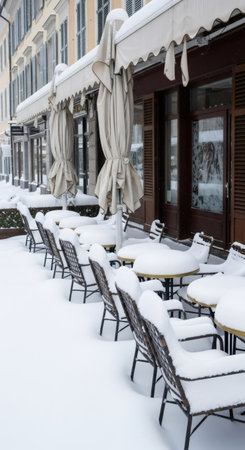 Outdoor cafe tables and chairs covered with snow on a city street in winter. Frozen city scene during cold weather with seasonal precipitation.の素材