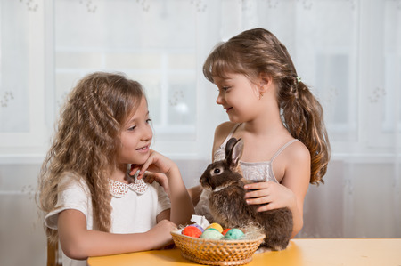 children play with a brown Easter Bunny. Next to them lay Easter eggsの写真素材