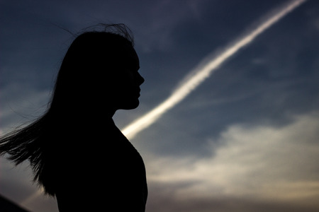 The silhouette of the girl against the evening blue sky and white strip from the planeの写真素材