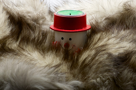 Snowman candle in scarf and red hat in furs