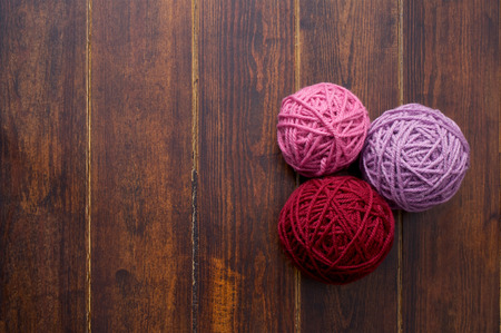 Three skeins in red and pink tones over wooden brown striped tableの写真素材