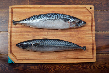 Two mackerels on wooden plate over brown wooden table
