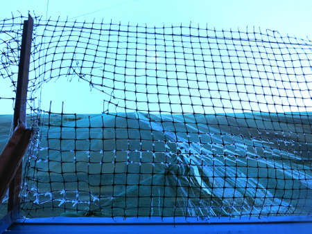 Torn grid fence for a house with a blue sky, icicles hanging from the gridの写真素材
