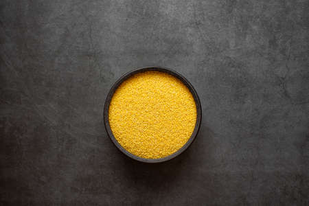 Yellow millet in spoon and bowl on dark grey background.の写真素材