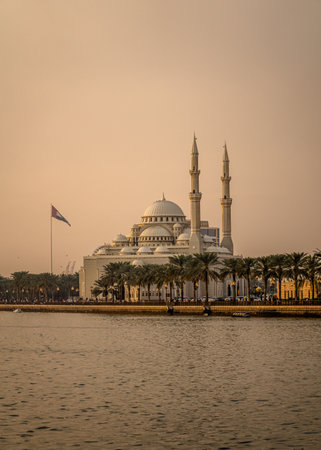 In the foreground, a mosque proudly displays a vibrant flag, while in the serene background, a tranquil body of water reflects the beauty around itの写真素材