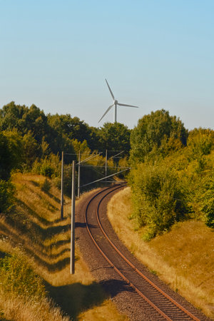 In a picturesque rural area, there is a train track stretching out with a large wind turbine prominently visible in the backgroundの写真素材