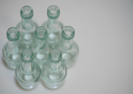 overhead cluster of glass bottles arranged on neutral surface, green-tinted clear glass necks form repeatingの写真素材