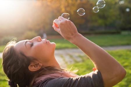 Beautiful yopung brunette girl blowing soap bubbles into the wind.