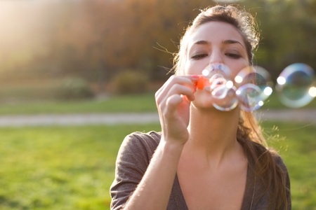 Beautiful yopung brunette girl blowing soap bubbles into the wind.の写真素材