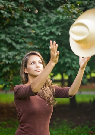 Beautilful young brunette posing outdoors, fooling around with her straw hat.の写真素材