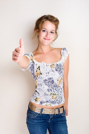 Half figure portrait of a cheerful fashionable young blond woman showing thumbs up.の写真素材