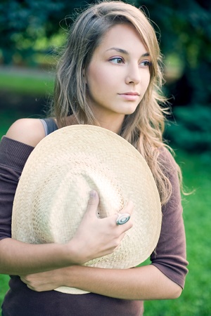 Portrait of beautiful dreamy brunette woman in the park holding straw hat.の写真素材