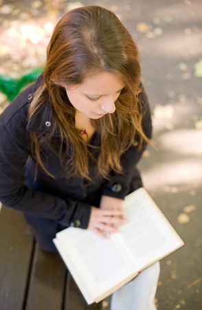 Portrait of beautiful young brunette girl reading a book in the park at fall.の写真素材