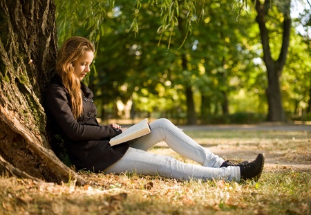 Portrait of beautiful young brunette girl reading a book in the park at fall.の写真素材