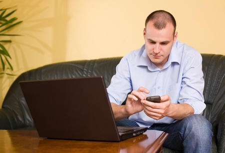 Casually dressed young businessman using mobile phone and laptop.の写真素材