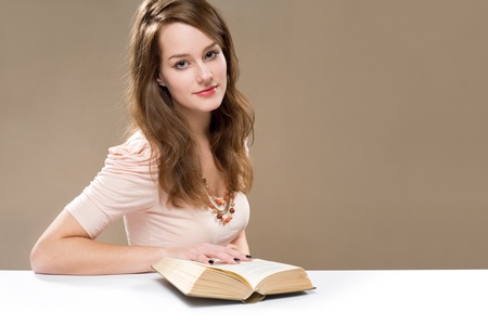 Gorgeous young brunette woman sitting at a white table reading a book.の写真素材